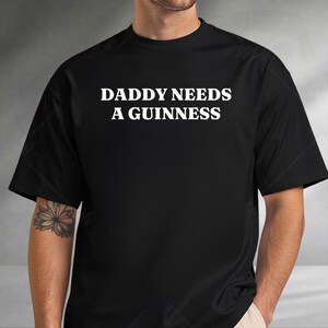 A man wearing a black t-shirt with the text "DADDY NEEDS A GUINNESS" printed on it.