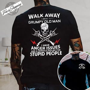May include: Black t-shirt with a graphic design featuring a skull, crossed bones, and the text "WALK AWAY I AM A GRUMPY OLD MAN". The shirt also includes the phrases "I HAVE ANGER ISSUES" and "STUPID PEOPLE".