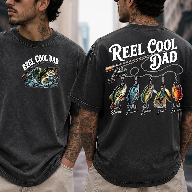 two men wearing black t-shirts with a fishing-themed design. The t-shirt on the left has a fish graphic and the text "REEL COOL DAD" above it, while the t-shirt on the right has a fishing rod and the text "REEL COOL DAD" above it.