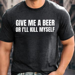 May include: Dark gray t-shirt with the white text "GIVE ME A BEER OR I'LL KILL MYSELF". The shirt has a crew neck and short sleeves. The text is centered on the chest.