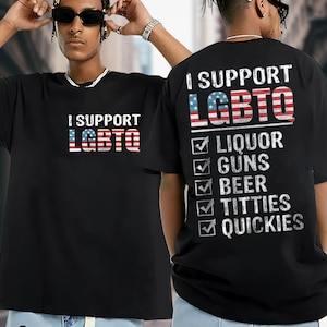 May include: Black t-shirts with the text "I SUPPORT LGBTQ" in white, with the letters filled with a red, white, and blue American flag design. The back of one shirt lists "Liquor, Guns, Beer, Titties, Quickies" with checkmarks.