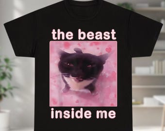 May include: Black t-shirt featuring a cat graphic with the text "the beast inside me" in pink. The cat is black and white, set against a pink background with heart shapes. The shirt is a classic crew neck.