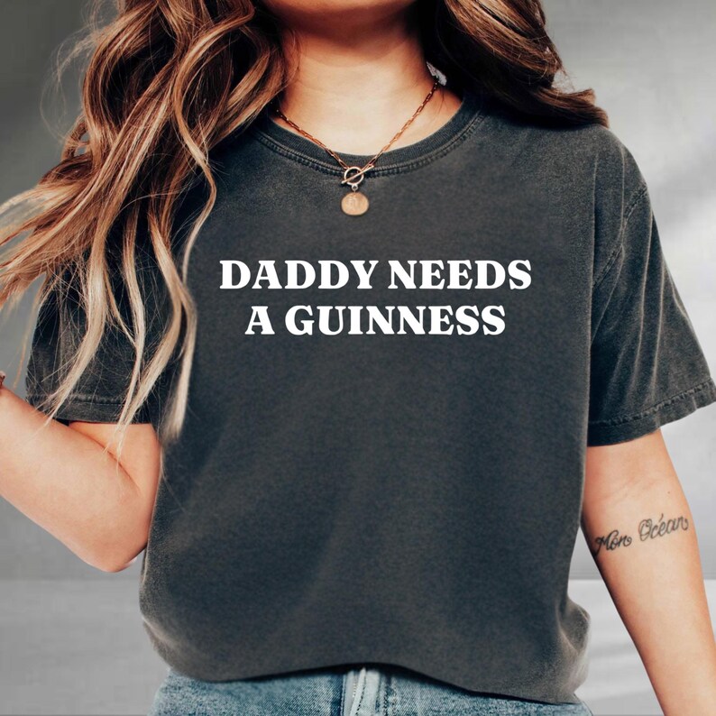 A person wearing a black t-shirt with the text "DADDY NEEDS A GUINNESS" printed on it.