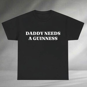 A black t-shirt with white text that says "DADMY NEEDS A GUINNESS".