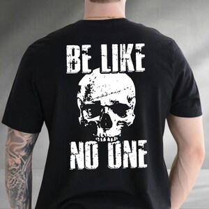 May include: Black t-shirt with a white skull graphic and the text "BE LIKE NO ONE". The design is centered on the back of the shirt. The shirt is made of a soft material.
