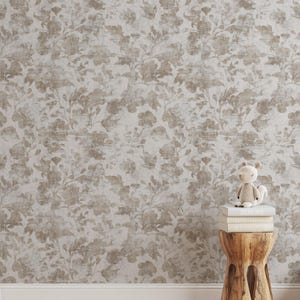 Puede incluir: Papel pintado floral en tonos neutros con un aspecto envejecido y texturizado. El diseño presenta grandes flores y follaje estilizados en tonos beige y topo sobre un fondo claro. Un pequeño taburete de madera sostiene libros y un peluche.