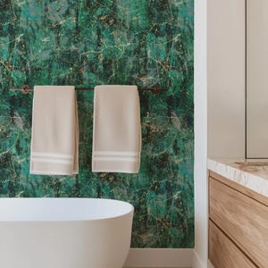 May include: A bathroom scene featuring a white bathtub and two beige towels hanging on a dark metal bar. The wall is adorned with a green and gold abstract pattern. A wooden vanity with a marble countertop is visible.