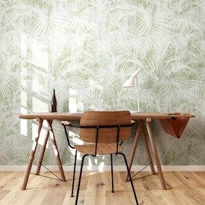 May include: A modern home office setup featuring a wooden desk, chair, and a white desk lamp. The background is a light green wallpaper with a white palm leaf pattern. A brown bottle sits on the desk.