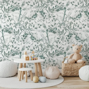 May include: A child's play area with a white table and stool, wooden toys, and a plush teddy bear in a wicker basket. The background features a green and white botanical wallpaper, with a white rug and floor cushions.