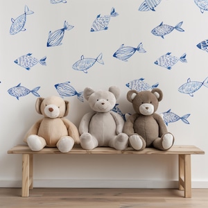 Könnte beinhalten: Drei Plüschbären, einer beige, einer grau und einer braun, sitzen auf einer Holzbank vor einer weißen Wand mit einem blauen Fischmuster.
