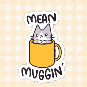 May include: A sticker with a cute cartoon cat in a yellow mug. The text on the sticker says "Mean Muggin'"