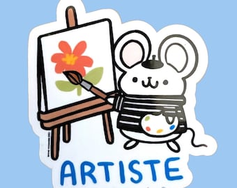 Può includere: Un adesivo raffigurante un topo bianco con una maglietta a righe bianche e nere e un basco, che tiene un pennello su una tela posta su un cavalletto. La tela mostra un fiore rosso. La parola ARTISTE è stampata in blu sotto il topo.