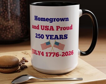 Könnte beinhalten: Weißer Keramikbecher mit schwarzem Innenraum und Henkel. Der Becher zeigt den Text "Homegrown and USA Proud 250 YEARS JULY4 1776-2026" in Blau und Rot, zusammen mit zwei amerikanischen Flaggen. Ein patriotischer Becher.