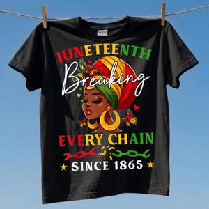 May include: Black t-shirt with a graphic celebrating Juneteenth. The design features a woman with a colorful head wrap, butterflies, and the words "Juneteenth Breaking Every Chain Since 1865" in red, green, and yellow.