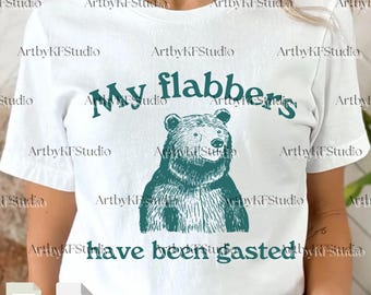 May include: White t-shirt with a teal graphic of a bear and the text "My flabbers have been gasted." The bear illustration is detailed, and the text is in a playful font. The shirt is a casual wear item.