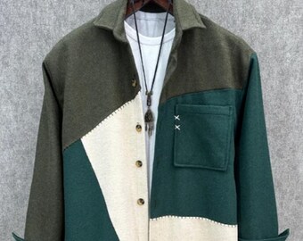 May include: A color-blocked shirt in shades of green and cream. The shirt features a collared neckline, button-down front, and a single pocket with decorative stitching. The sleeves are cuffed, and the shirt is displayed on a hanger against a neutral background.