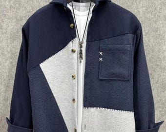 May include: A navy blue and gray patchwork jacket with a collared neckline and a single pocket. The jacket has a button-down front and long sleeves. A white t-shirt is visible underneath, and a necklace hangs from the collar.
