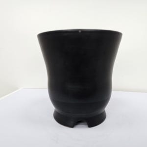 Pode incluir: Um vaso de cerâmica preta com a parte superior alargada e uma base arredondada. O acabamento escuro e fosco contrasta com a superfície branca sobre a qual está. O vaso tem uma forma curva única, adequado para uso interno ou externo.