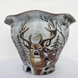Op de afbeelding: Een keramische plantenbak met een winterse scène met twee herten. De plantenbak heeft een gerimpelde rand en een lichtblauwe achtergrond met geschilderde bomen en vallende sneeuw. De herten zijn bruin met grote geweien.