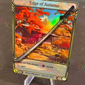 May include: A trading card titled "Edge of Autumn" featuring a miniature sword. The card has a gold border and a background image of autumn foliage. The sword is silver with a black handle and rests on a clear stand.