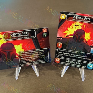 May include: Two trading cards featuring Boba Fett from the Star Wars universe. The cards are displayed on clear stands against a dark background. The cards have a red and black color scheme with character art and game text.