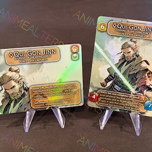 Puede incluir: Dos cartas coleccionables con Qui-Gon Jinn de Star Wars. Las cartas muestran ilustraciones del personaje, con texto como "Student of the Living Force" y mecánicas de juego. Las cartas se exhiben en soportes de plástico transparente.