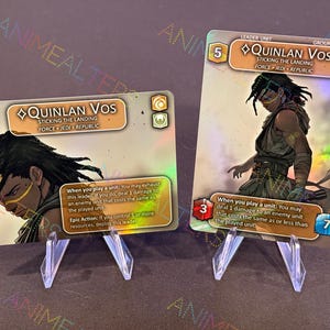 Puede incluir: Dos cartas de juego de comercio holográficas con Quinlan Vos de Star Wars: Destiny. Las cartas son doradas y azules con un efecto holográfico. El texto en las cartas dice "Quinlan Vos" y "Sticking the Landing".