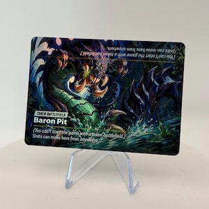 May include: A rectangular game card titled Baron Pit, featuring a green and purple monster emerging from water. The card text reads Token Battlefield and includes the rule: You can't start the game with a token battlefield. Units can move here from anywhere.