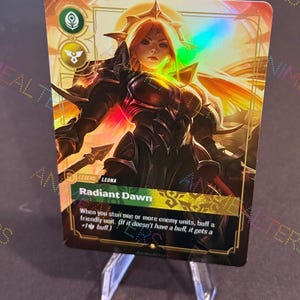 Puede incluir: Una tarjeta coleccionable holográfica que presenta a una guerrera con cabello rojo y armadura dorada, titulada "Radiant Dawn". La tarjeta tiene un borde dorado y negro con texto que describe una habilidad del juego. La tarjeta se muestra en un soporte de plástico transparente.