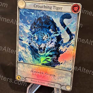 Może przedstawiać: Karta kolekcjonerska z ilustracją niebieskiego tygrysa i tekstem "Crouching Tiger". Karta ma srebrną obwódkę i zawiera tekst "Ephemeral. Go again" oraz "Ninja Action - Attack".