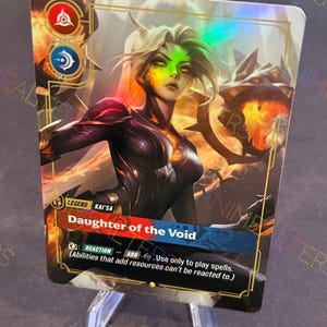 以下が含まれることがあります： 緑とブロンドの髪、暗い衣装の女性キャラクターが描かれたホログラフィックトレーディングカード。「Daughter of the Void」と「Kai'Sa」の文字と、反応と能力に関するテキストが書かれています。カードは透明なスタンドに表示されています。