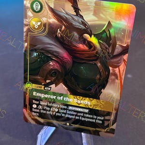 Op de afbeelding: Een holografische ruilkaart met het personage Azir, de Keizer van de Zanden, met een gedetailleerde illustratie van een krijger in harnas. De kaart heeft gouden accenten en de tekst "Emperor of the Sands".