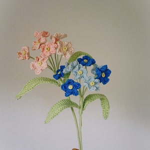 May include: A bunch of crocheted flowers in pink, blue, and light blue. The flowers are arranged in a bouquet and have green stems.