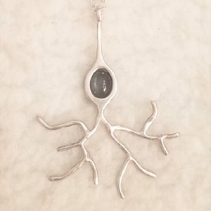 May include: A silver necklace with a neuron pendant. The neuron is made of silver and has a dark gray stone in the center.