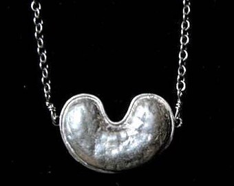 May include: A silver necklace with a bean-shaped pendant. The pendant has a hammered texture and a smooth, polished finish.