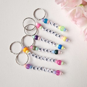 May include: Six colourful beaded keychains with names spelled out in white letters. The names are Leo, Harper, Lucas, Noah, Charlotte, and Evelyn.