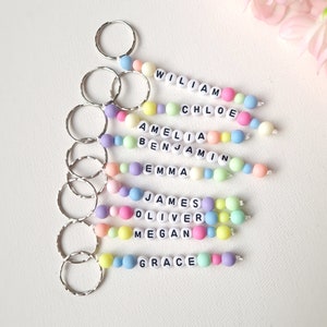May include: A set of eight colorful beaded keychains with names spelled out in white letters. The names are William, Chloe, Amelia, Benjamin, Emma, James, Oliver, Megan, and Grace.