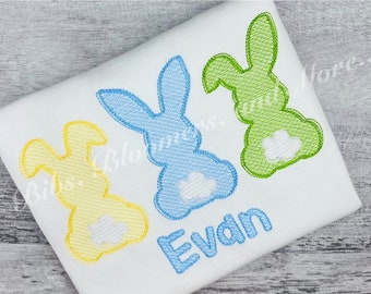 May include: A white t-shirt with three embroidered bunny silhouettes in yellow, blue, and green. The bunnies have white embroidered tails. The name "Evan" is embroidered in blue below the bunnies.