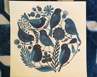 Op de afbeelding: Een blauwe en witte print van een cirkel met blauwe vogels en bloemen. De vogels zijn gestileerd en hebben een folk art-uitstraling. De bloemen zijn ook gestileerd en hebben een speelse uitstraling.