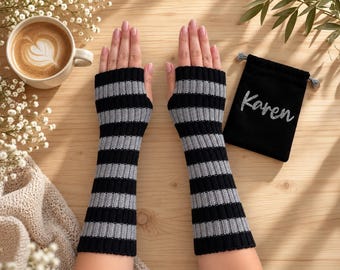 May include: A pair of fingerless arm warmers featuring a ribbed knit pattern with alternating horizontal black and grey stripes. Beside the arm warmers is a small black drawstring pouch with the name Karen embroidered in a silver script font.