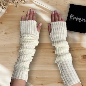 Peut inclure: Une paire de mitaines blanches en tricot avec une texture côtelée. Les mitaines sont longues et dépassent le poignet.