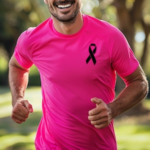 May include: A pink running shirt with a black ribbon on the front. The shirt is made of a breathable material and is perfect for working out or running.