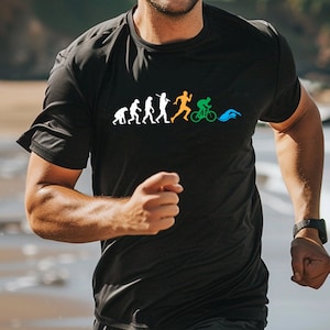 May include: A black t-shirt featuring a graphic of the evolution of a triathlete. The graphic depicts a stick figure evolving from a caveman to a runner, then a cyclist, and finally a swimmer.