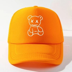 May include: Orange mesh trucker hat with a white graphic of a cartoon bear with an X for eyes and a smile.