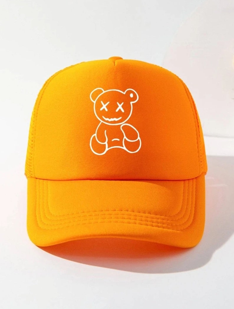 May include: Orange mesh trucker hat with a white graphic of a cartoon bear with an X for eyes and a smile.