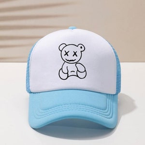May include: A white and light blue trucker hat with a black and white cartoon bear with X's for eyes.