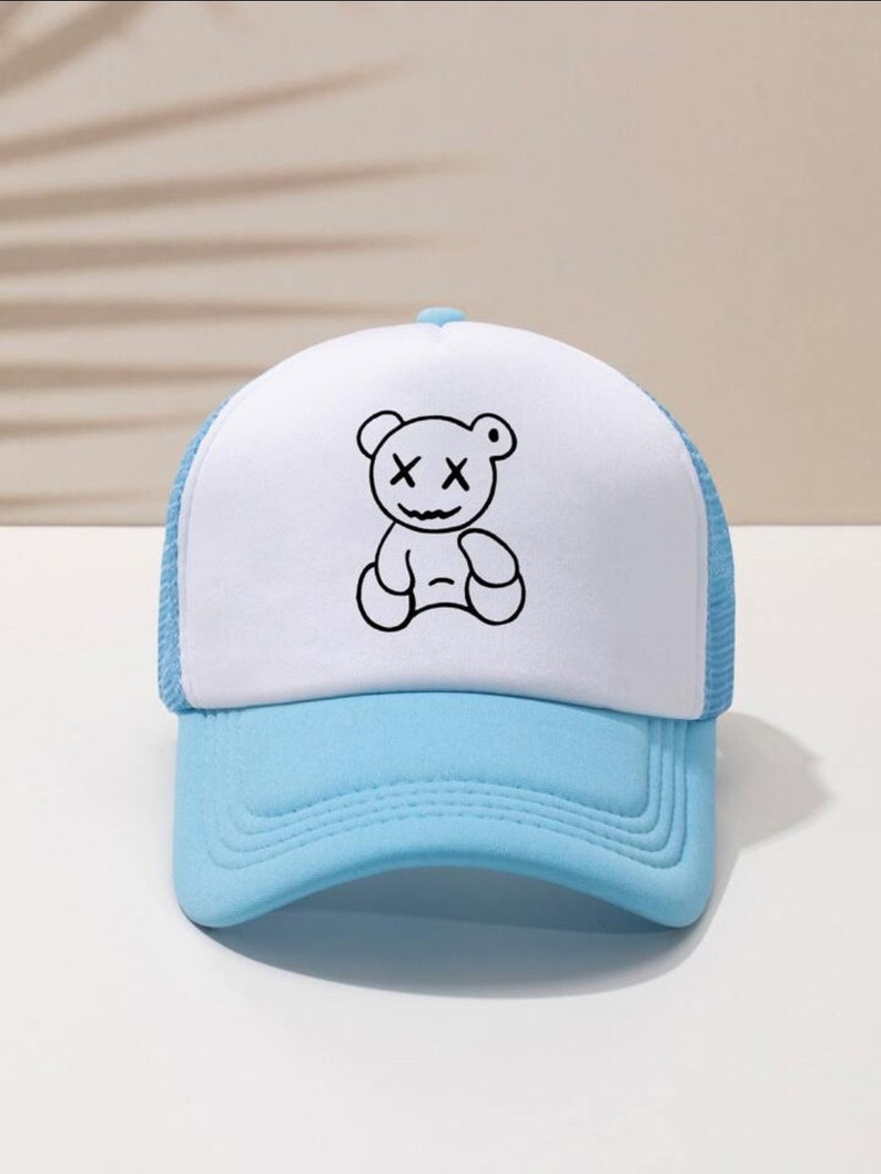 May include: A white and light blue trucker hat with a black and white cartoon bear with X's for eyes.