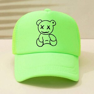 May include: A neon green trucker hat with a black outline of a teddy bear with an X for eyes.