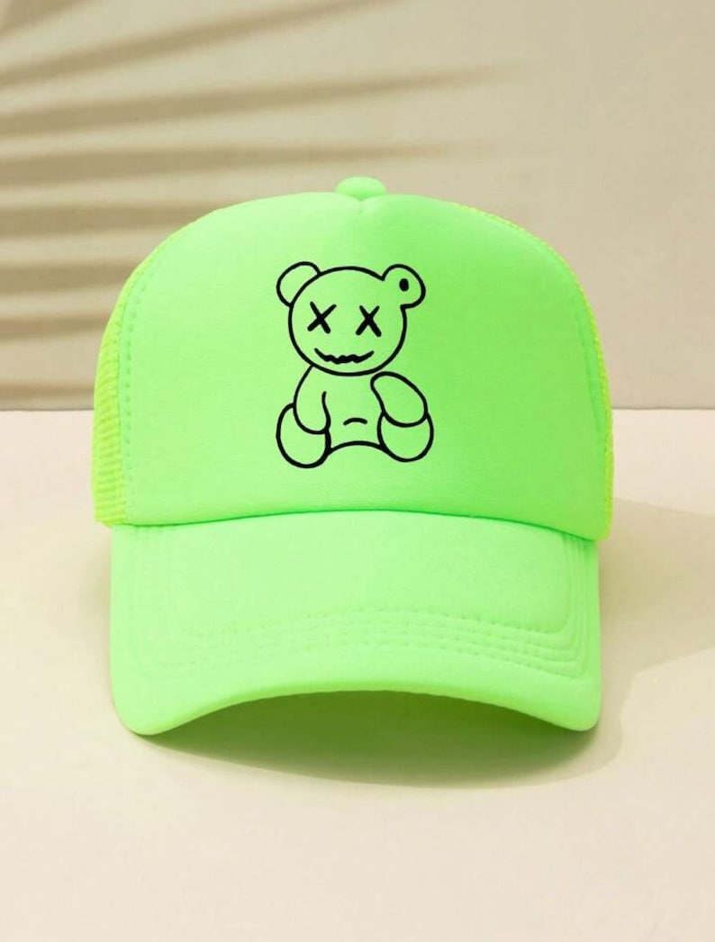 May include: A neon green trucker hat with a black outline of a teddy bear with an X for eyes.