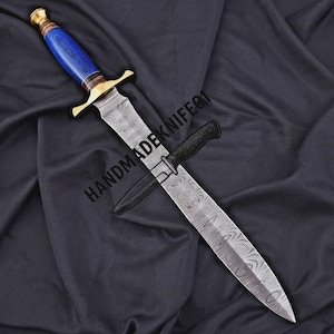 May include: A handmade dagger with a patterned blade and a blue and gold handle. The dagger is accompanied by a smaller knife in a sheath. The text "HANDMADENIFE01" is printed on the blade.